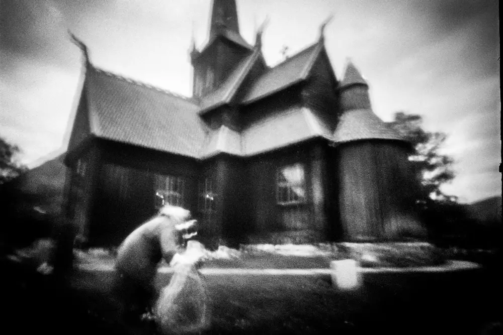 A pinhole shot of an old woman laying flowers on a grave in a Norwegian churchyard. 
