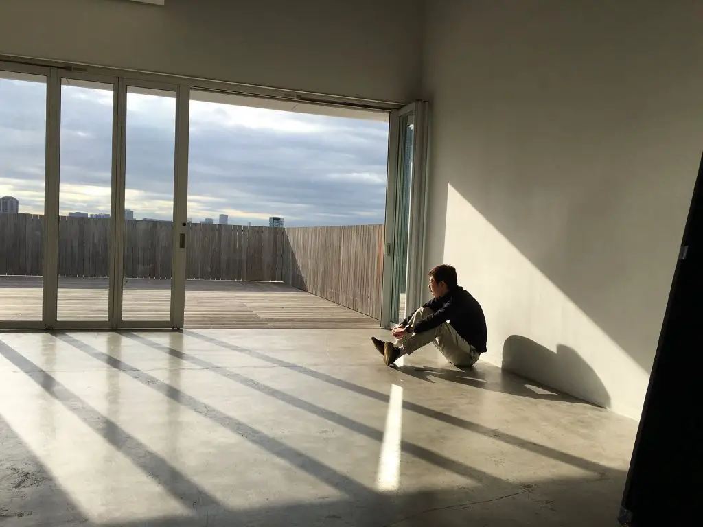 a man sits in an empty room looking out of the window