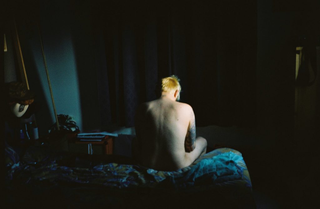 a naked person sitting on the edge of a bed facing away from us