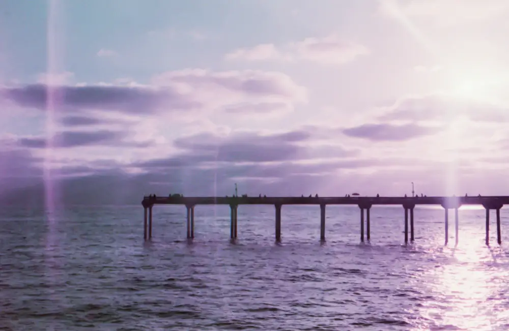 a pier jutting out into the ocean with a purple tinged sky