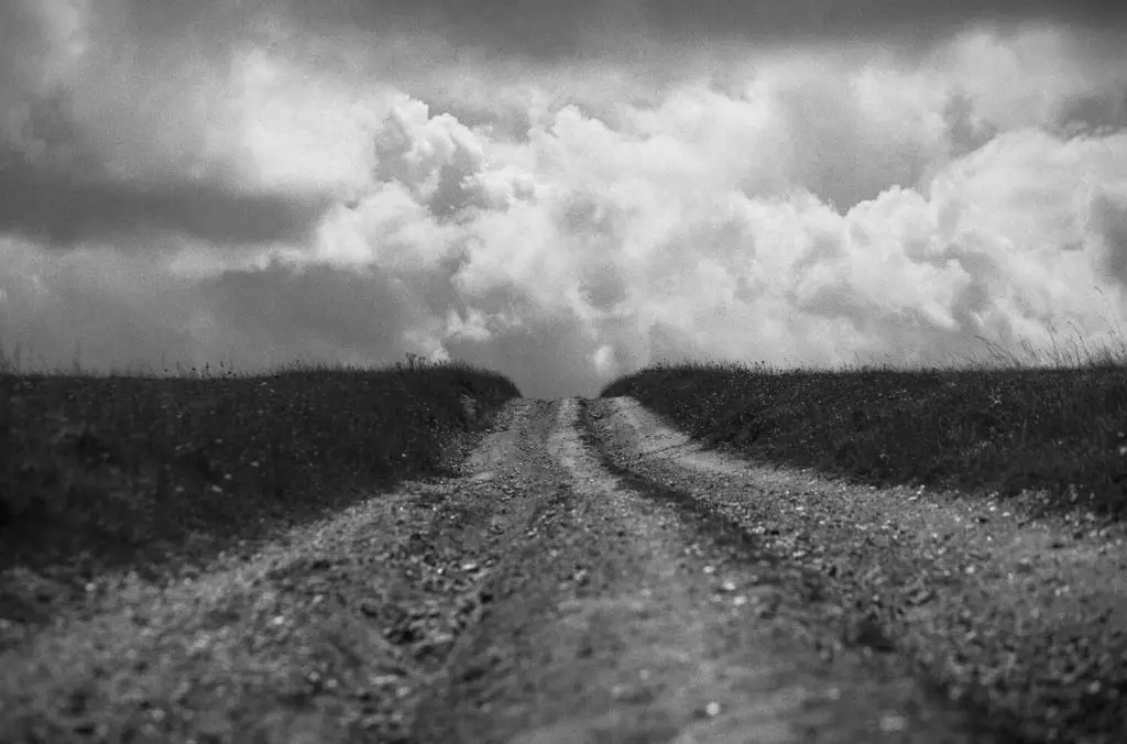 A low-angle view of a chalk path which leads straight ahead to the horizon with a cloudy sky above.