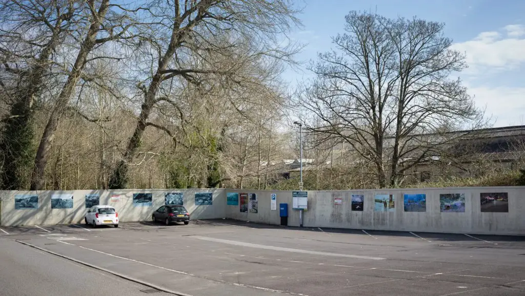 An almost empty open-air car park with the Saxonvale prints on display on hoardings along two sides of the car park.