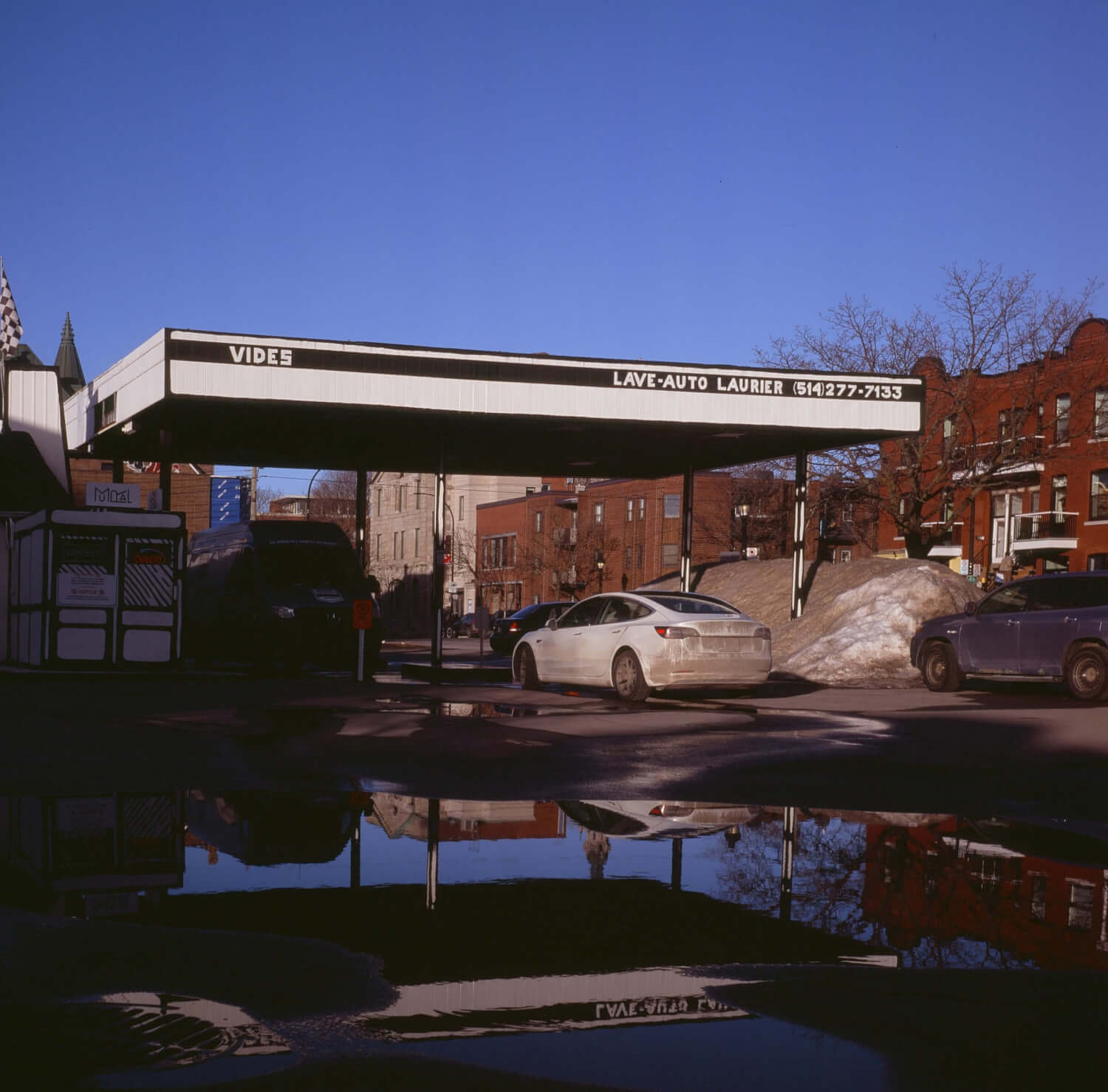 Image of a car wash with a large puddle in the foreground. The sky is blue in the background. 